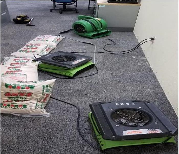 Office space with SERVPRO air movers and sandbags fighting intruding moisture. 